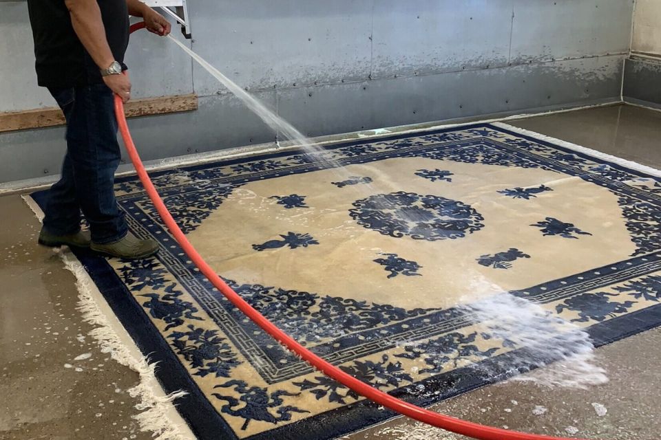 A man cleans a rug with a hose, highlighting a rug cleaning service based in Washington, DC.