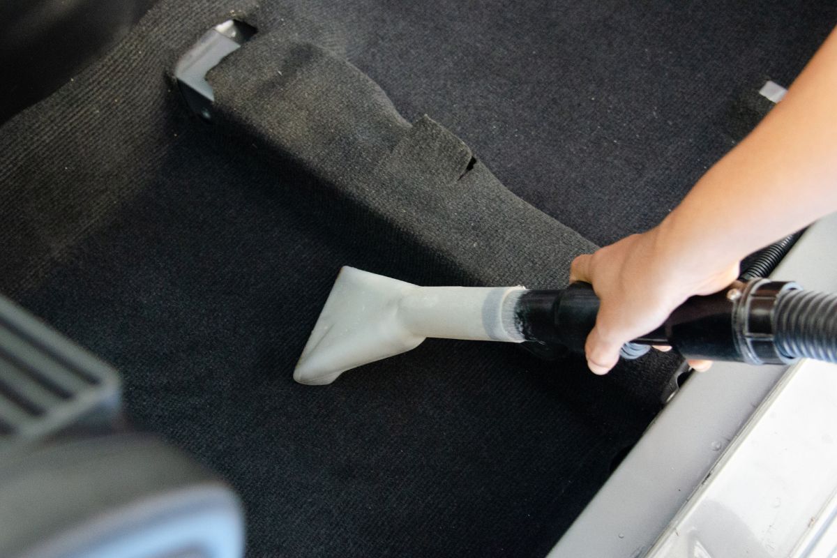 A person operates a vacuum cleaner inside a car, cleaning the floor and upholstery for a tidy interior.