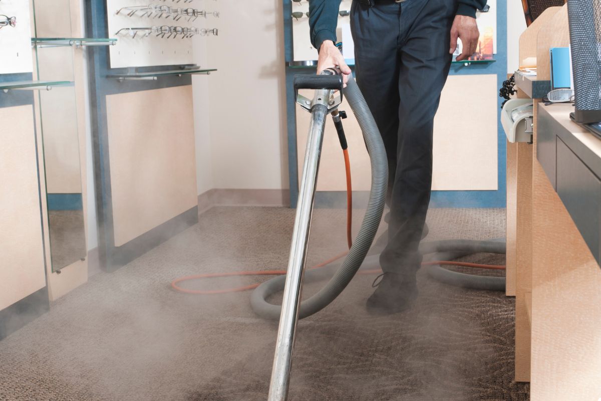A man operates a vacuum cleaner on a carpet, focusing on removing dirt and debris from the surface.