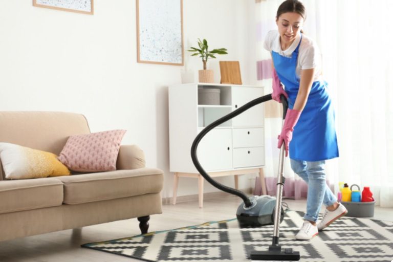 A woman wearing an apron is actively cleaning a room, using a cloth to wipe surfaces.